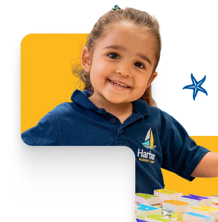 Smiling preschooler playing with letter blocks at Harbor Preschool Academy